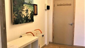 A hallway with a wooden floor, a white bench with a basket, a door, and a painting of palm trees. - Splendid 1 Bedroom Flat + Terrace (Kentish Town) (London)