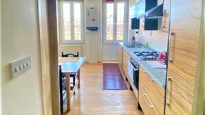 A narrow kitchen with wooden cabinets, a dining table, and a red pendant light. - Splendid 1 Bedroom Flat + Terrace (Kentish Town) (London)