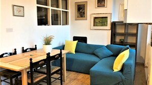 A cozy living room with a wooden dining table, blue sofa, and yellow cushions. - Splendid 1 Bedroom Flat + Terrace (Kentish Town) (London)
