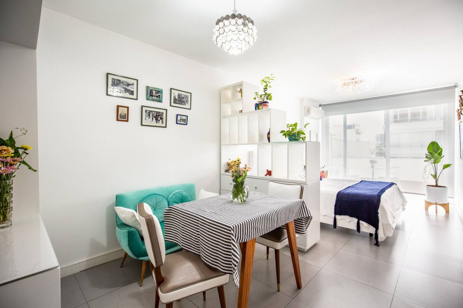 Un espace repas moderne avec une nappe à rayures, un canapé turquoise et un meuble blanc orné de plantes.
