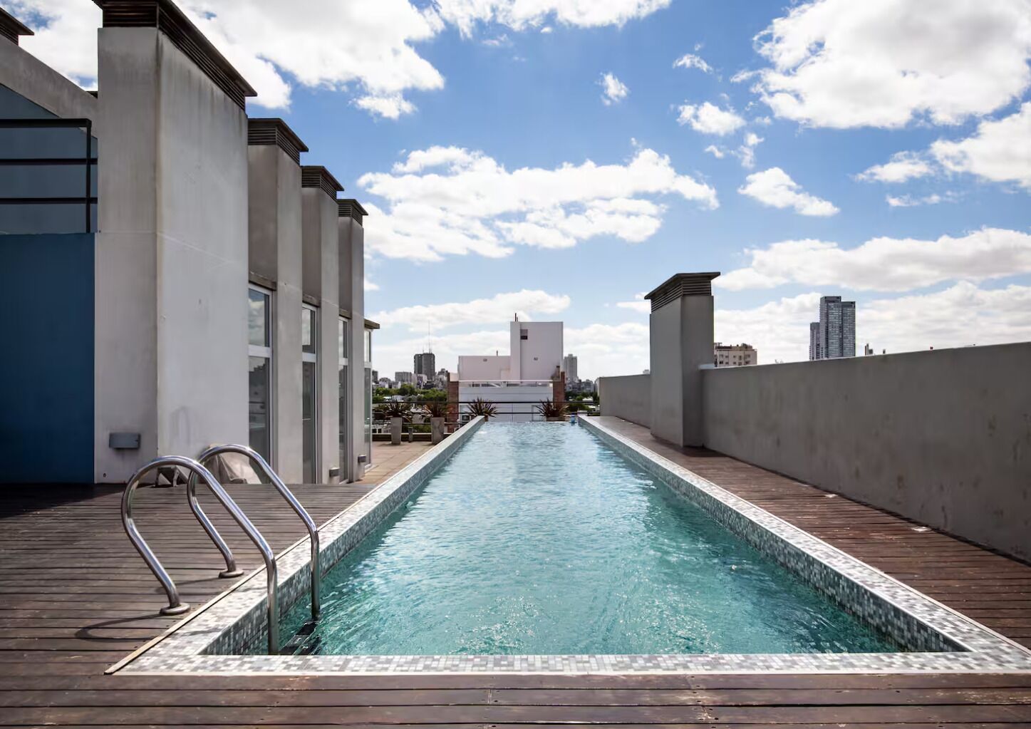 Ein Dachpool mit Holzterrasse, Metallgeländern und Blick auf die Stadt.