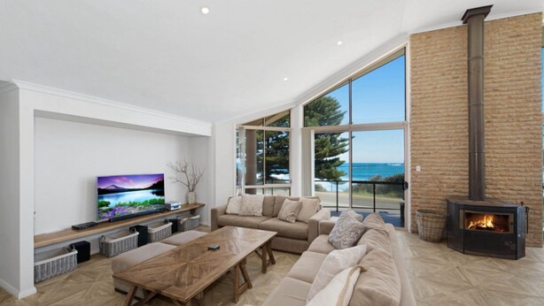 A modern living room with a large TV, comfortable seating, a fireplace, and a view of the sea. - Siesta by the Sea - Beachside Retreat (COPACABANA)