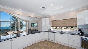 A modern kitchen with white cabinets, a black countertop, and a large window with a view of the ocean. - Siesta by the Sea - Beachside Retreat (COPACABANA)