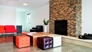 A modern living room with a brick fireplace, red and black ottomans, and a white coffee table.