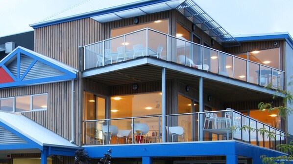 A modern building with a glass balcony, multiple seating areas, and a staircase leading to an upper level.