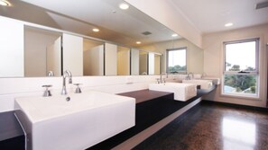 A modern bathroom with three sinks, large mirrors, and a window providing natural light.