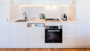 Una cocina moderna con gabinetes blancos, lavavajillas de acero inoxidable, horno empotrado, estufa a gas y máquina de café.