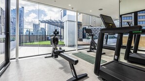 A modern gym with exercise equipment, large windows, and a view of the cityscape.