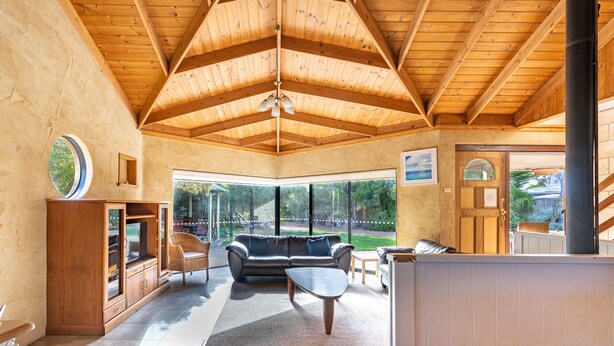 A spacious living area with a high wooden ceiling, large windows, a sofa, and a coffee table.