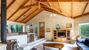 A spacious living room with a high wooden ceiling, a fireplace, a television, and a cozy seating area.