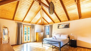 A bedroom with a wooden ceiling, a bed, a dresser, a mirror, and a window with curtains.
