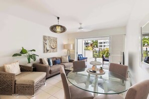 A modern living room with a glass dining table, wicker furniture, and a view to the outside.