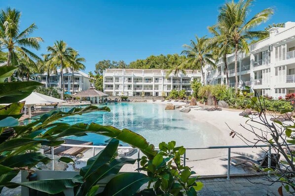 A hotel with a pool, palm trees, and a beach area.