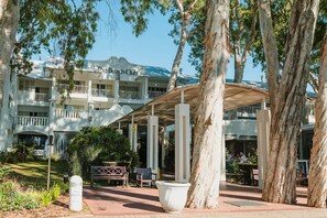 A multi-story hotel with a covered outdoor seating area, trees, and a sign reading 'The Beach Club.'