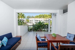 A balcony with a view of a building, a wooden table with chairs, and a blue sofa.