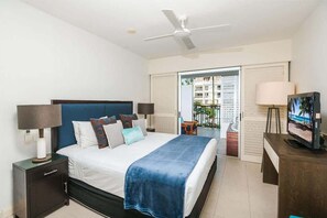 Ein Schlafzimmer mit Bett, Nachttischen, Deckenventilator, Fernseher und Blick ins Freie.
