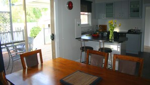 A dining area with a wooden table and chairs, a kitchen with white cabinets, and a view of the outdoors through a sliding door. - Banksia Cottage - An Old Charm Cottage that has been completely renovated (Albury)