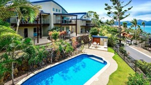Una casa moderna de dos pisos con piscina, rodeada de vegetación tropical y vista al océano.