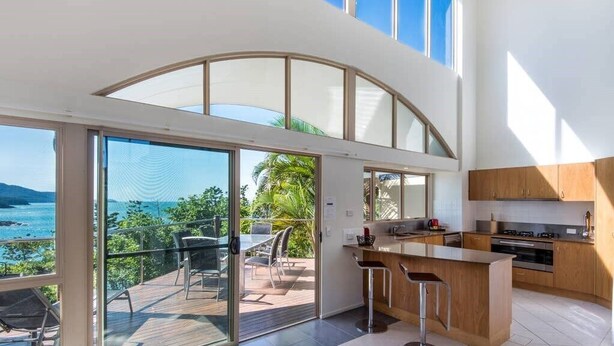 Una cocina moderna con una isla grande, una puerta corrediza de vidrio que da a una terraza exterior y vistas al mar.