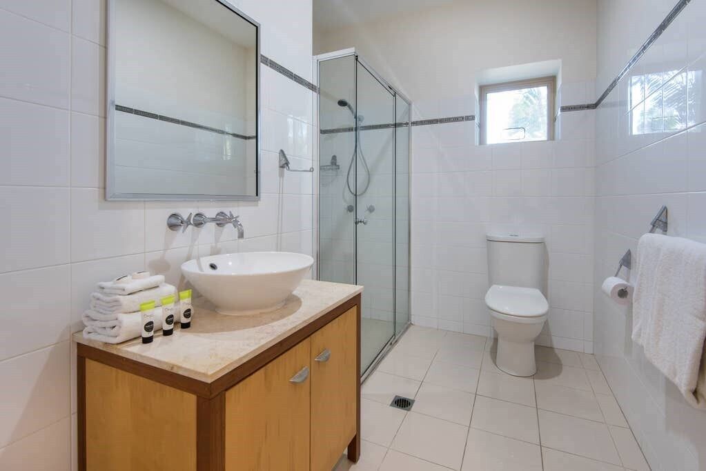 Un baño moderno con ducha de vidrio, un lavabo blanco y un inodoro.
