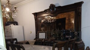 Ein Esszimmer mit einem großen Tisch, Holzsesseln, einer Kristallleuchtre und einem Vintage-Radio.