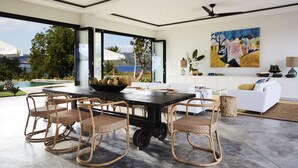 Un comedor moderno con una mesa negra, sillas de mimbre y vistas a una piscina y follaje.
