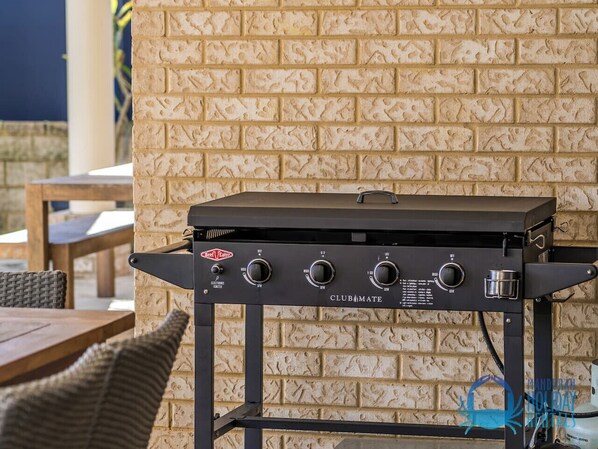 A barbecue grill with four controls, branded 'ClubMate', against a brick wall.