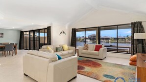 A spacious living room with two sofas, a dining area, and large windows offering a view of the water. - Canal Elegance in Yunderup (South Yunderup)