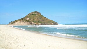 A beach with a prominent hill in the background. - VistaMar at Villa del Sol Residences (Recreio dos Bandeirantes)