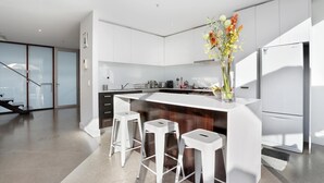 A modern kitchen with white cabinets, a central island with stools, a refrigerator, and a vase with flowers.