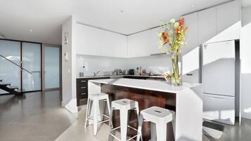 A modern kitchen with white cabinets, a central island with stools, a refrigerator, and a vase with flowers.