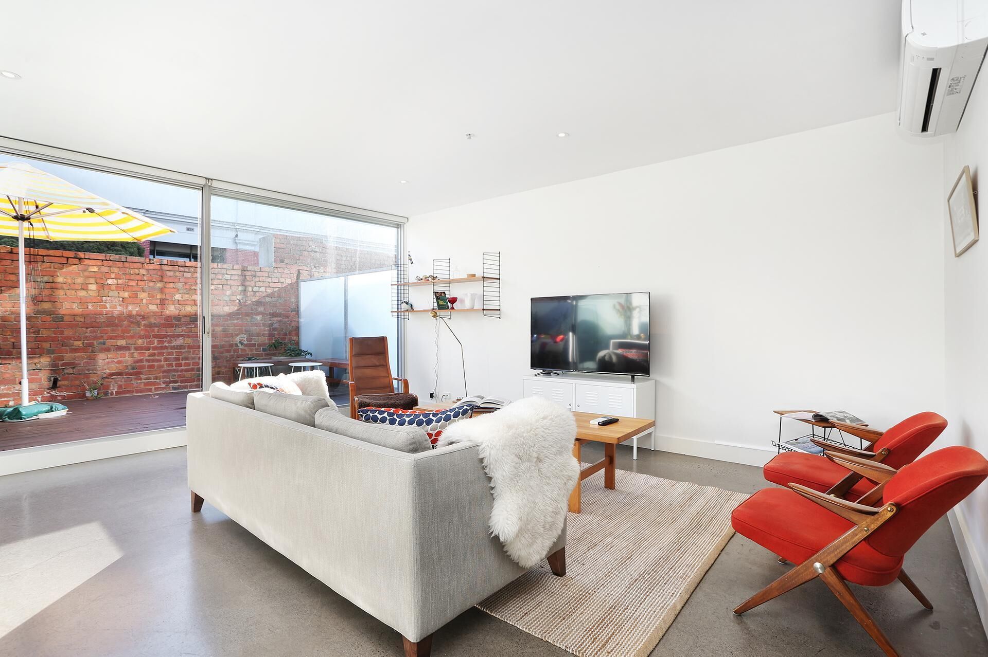 A modern living room with a large window, a sofa, a TV, and red chairs.