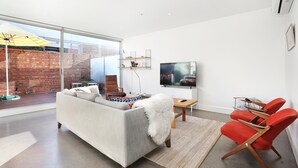 A modern living room with a large window, a sofa, a TV, and red chairs.