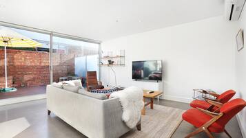 A modern living room with a large window, a sofa, a TV, and red chairs.