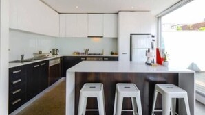 A modern kitchen with white cabinets, a central island with stools, and a large window providing natural light.