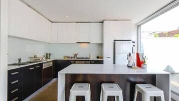 A modern kitchen with white cabinets, a central island with stools, and a large window providing natural light.