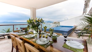 Una mesa de comedor dispuesta con platos, cubiertos y vasos, con vistas a una piscina y un paisaje pintoresco.