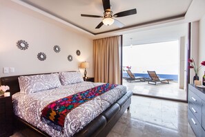 Habitación de hotel con una cama grande, ventilador de techo, espejos decorativos en la pared, balcón con vistas y mesita de noche con lámpara.