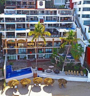 Un hotel de varios pisos con balcones, zona de piscina y mobiliario exterior.