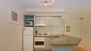 Una cocina compacta equipada con refrigerador, microondas y horno, además de una pequeña isla con pileta.