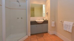Un baño con cabina de ducha de vidrio, un lavamanos con espejo y un perchero para toallas.
