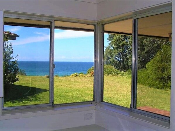 A room with large windows offering a view of the sea and a grassy landscape. - A little beach front cottage (Culburra Beach)