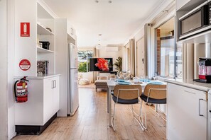 A modern kitchen with a dining area, a fire extinguisher, and a television. - A little beach front cottage (Culburra Beach)