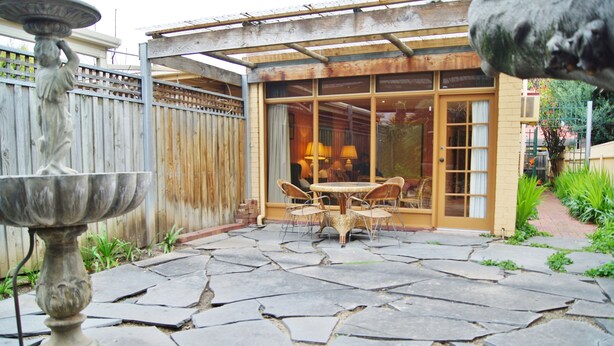 Une terrasse avec un sol en pierre, un coin repas avec des chaises et une table, et une statue.