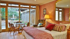 Une chambre d’hôtel comprenant un lit, un coin salon avec une table et des chaises, une grande fenêtre et une porte donnant sur un espace extérieur.