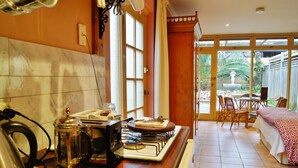 Une cuisine équipée d’une cuisinière, d’une bouilloire et d’une machine à café, un coin repas avec une table et des chaises, et une chambre avec un lit et des rideaux.