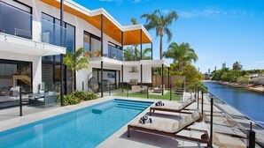 A modern house with a swimming pool, lounge chairs, and a view of the water. - Relax, Chill, Enjoy and Luxury all comes in this Property! (Gold Coast)