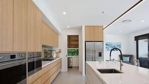 A modern kitchen with wooden cabinets, stainless steel appliances, and a large island with a sink. - Relax, Chill, Enjoy and Luxury all comes in this Property! (Gold Coast)
