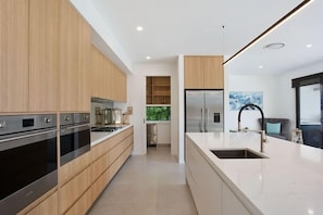 A modern kitchen with wooden cabinets, stainless steel appliances, and a large island with a sink. - Relax, Chill, Enjoy and Luxury all comes in this Property! (Gold Coast)