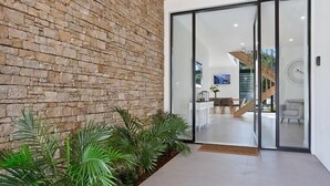 A modern interior with a stone wall, sliding glass doors leading to a dining area, and indoor plants. - Relax, Chill, Enjoy and Luxury all comes in this Property! (Gold Coast)
